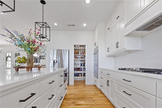 kitchen featuring appliances with stainless steel finishes, light wood-type flooring, backsplash, white cabinets, and hanging light fixtures