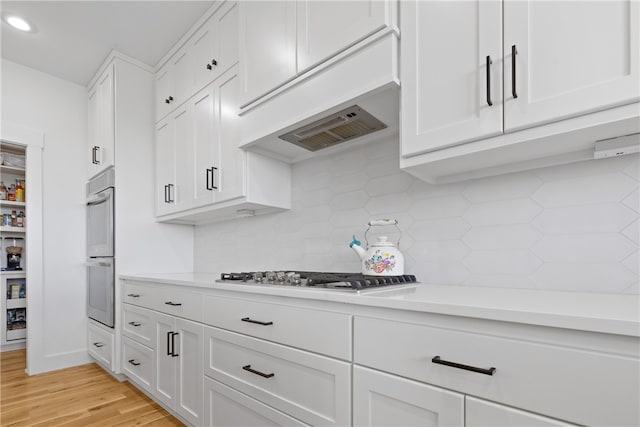 kitchen with double wall oven, white cabinets, light hardwood / wood-style floors, and stainless steel gas stovetop