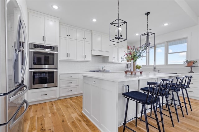 kitchen with a kitchen bar, stainless steel appliances, light hardwood / wood-style flooring, white cabinets, and a center island