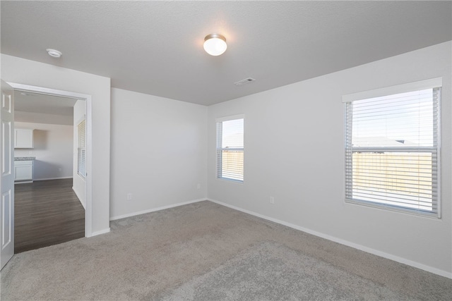 spare room with a healthy amount of sunlight, a textured ceiling, and dark carpet