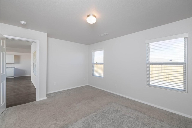 carpeted spare room featuring baseboards and visible vents