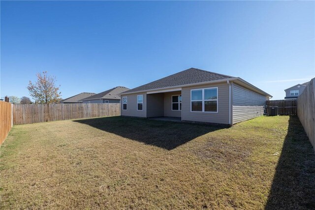 rear view of house featuring a yard, a fenced backyard, and roof with shingles