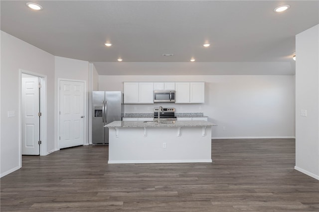 kitchen with light stone countertops, stainless steel appliances, dark wood-type flooring, a center island with sink, and white cabinetry