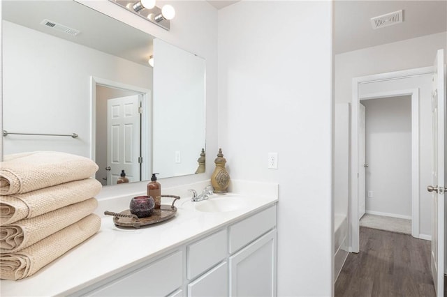 bathroom featuring visible vents, wood finished floors, vanity, and a bath