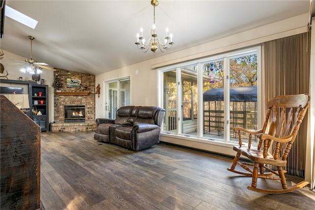 living room with lofted ceiling with skylight, a fireplace, ceiling fan with notable chandelier, and dark hardwood / wood-style floors