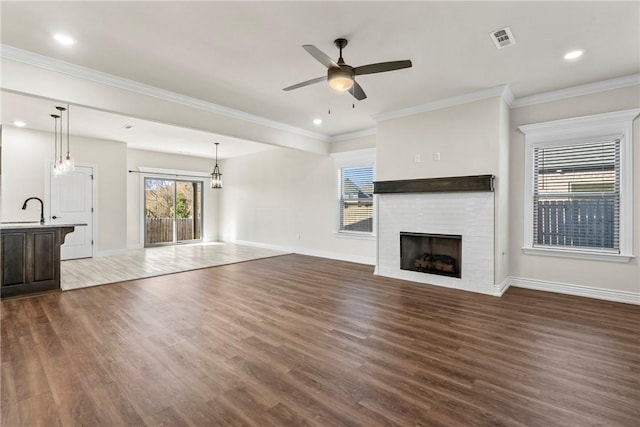 unfurnished living room featuring wood-type flooring, sink, ceiling fan with notable chandelier, and ornamental molding