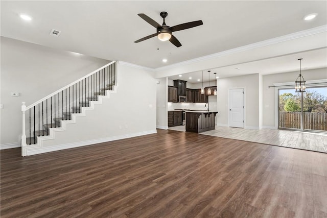 unfurnished living room with ornamental molding, ceiling fan with notable chandelier, and dark hardwood / wood-style flooring