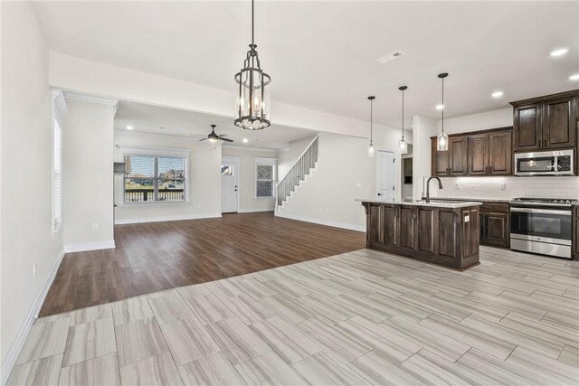 kitchen with sink, decorative light fixtures, dark brown cabinets, appliances with stainless steel finishes, and a kitchen island with sink