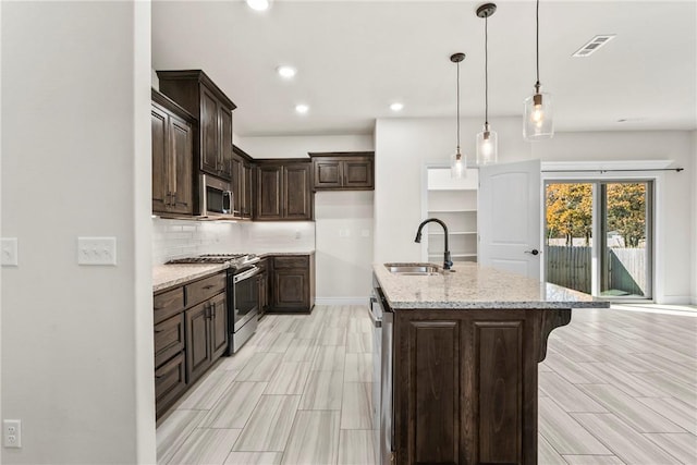 kitchen featuring sink, hanging light fixtures, stainless steel appliances, light stone countertops, and an island with sink