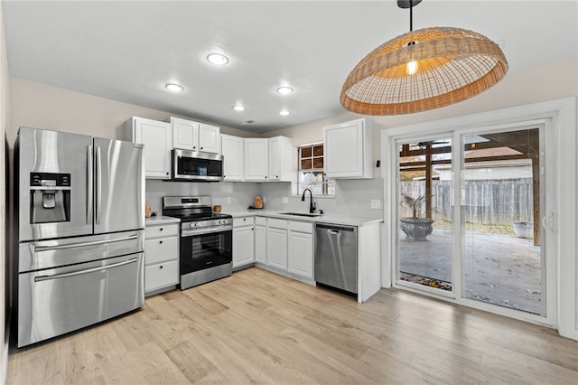 kitchen featuring appliances with stainless steel finishes, light wood-type flooring, sink, white cabinets, and hanging light fixtures