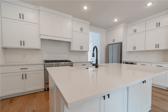 kitchen with white cabinets, an island with sink, light wood-type flooring, and appliances with stainless steel finishes