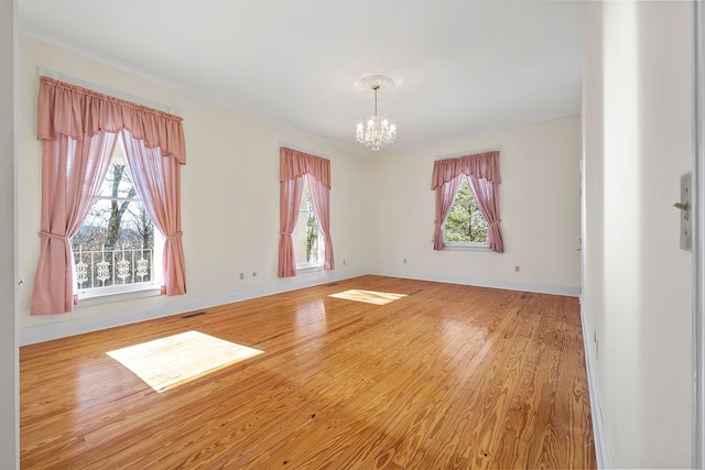 empty room with hardwood / wood-style flooring, plenty of natural light, and a notable chandelier