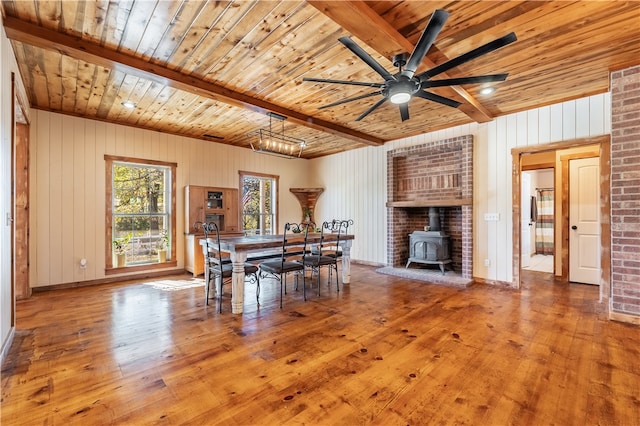 unfurnished dining area with beam ceiling, a wood stove, wooden ceiling, wooden walls, and hardwood / wood-style flooring