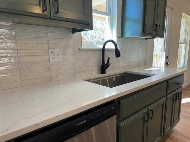 kitchen featuring sink, stainless steel dishwasher, decorative backsplash, light wood-type flooring, and light stone counters