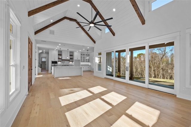 unfurnished living room with beam ceiling, light wood-type flooring, high vaulted ceiling, and ceiling fan