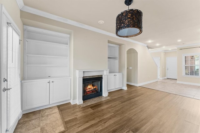 unfurnished living room with built in features, wood-type flooring, and crown molding