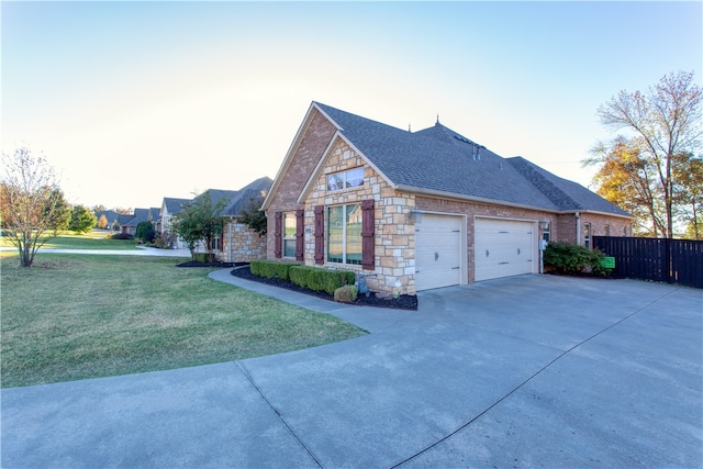 view of side of home with a garage, fence, driveway, stone siding, and a lawn