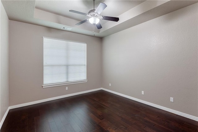 empty room featuring dark wood-style flooring, a raised ceiling, visible vents, ceiling fan, and baseboards