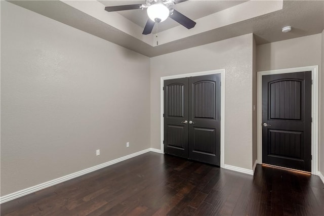 unfurnished bedroom with dark wood-type flooring, a ceiling fan, baseboards, a closet, and a raised ceiling