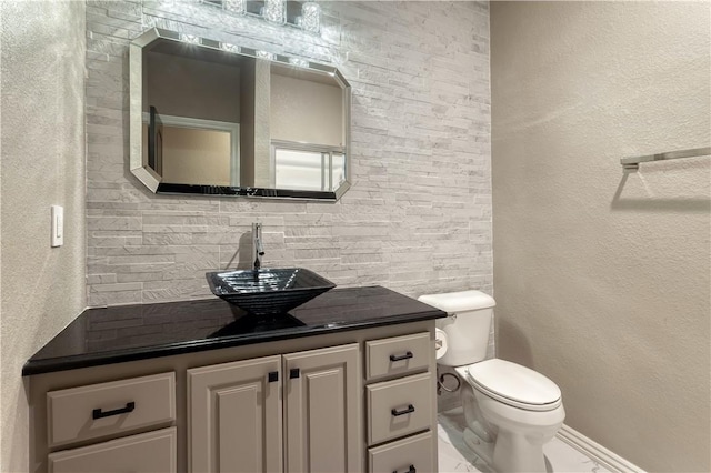 half bath featuring tasteful backsplash, a textured wall, vanity, and toilet