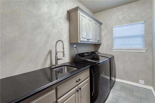 clothes washing area with cabinet space, baseboards, a textured wall, separate washer and dryer, and a sink