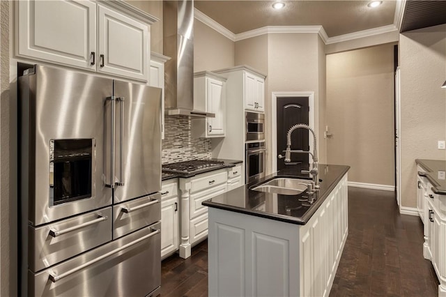 kitchen featuring dark countertops, wall chimney exhaust hood, stainless steel appliances, crown molding, and a sink