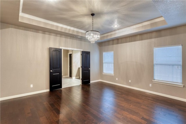 empty room with a notable chandelier, dark wood finished floors, baseboards, a raised ceiling, and crown molding