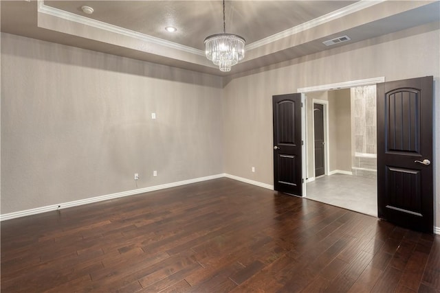 unfurnished room with visible vents, ornamental molding, dark wood-style floors, a tray ceiling, and an inviting chandelier