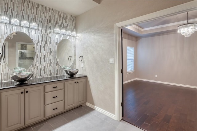 bathroom with double vanity, baseboards, a sink, an inviting chandelier, and backsplash