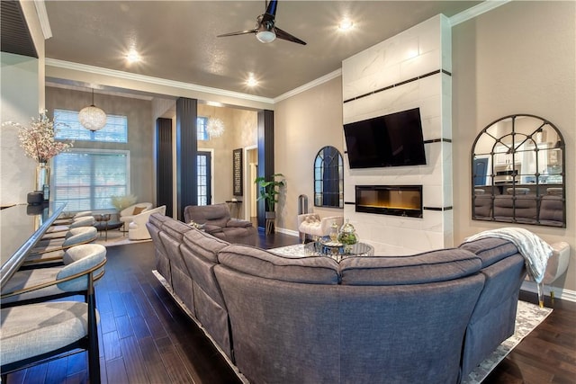 living area with a ceiling fan, baseboards, a tiled fireplace, dark wood finished floors, and crown molding