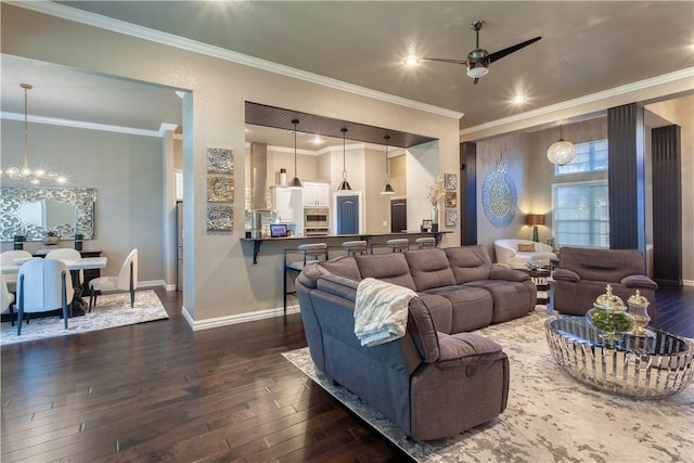 living area with dark wood-type flooring, crown molding, baseboards, and ceiling fan with notable chandelier