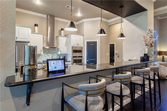 kitchen with a breakfast bar area, stainless steel appliances, visible vents, wall chimney range hood, and dark wood-style floors