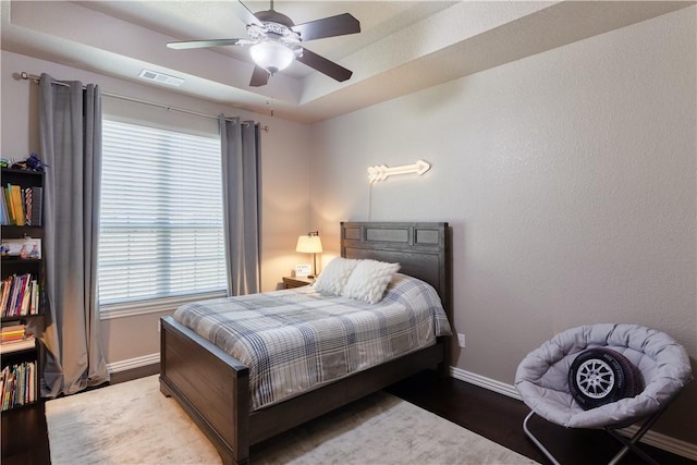 bedroom with baseboards, visible vents, a ceiling fan, wood finished floors, and a tray ceiling