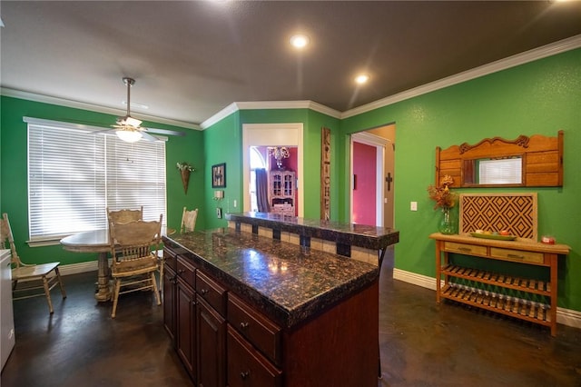 kitchen featuring dark brown cabinets, ornamental molding, a kitchen island, ceiling fan, and dark stone counters