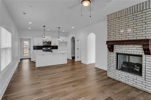 unfurnished living room featuring hardwood / wood-style floors, ceiling fan, sink, and a brick fireplace