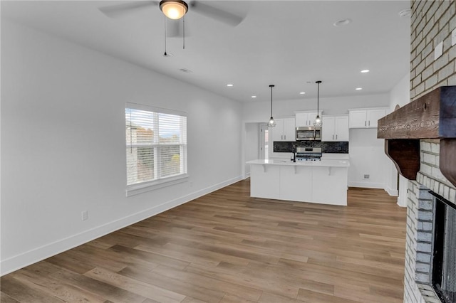 kitchen with hanging light fixtures, stainless steel appliances, a fireplace, white cabinets, and a center island with sink