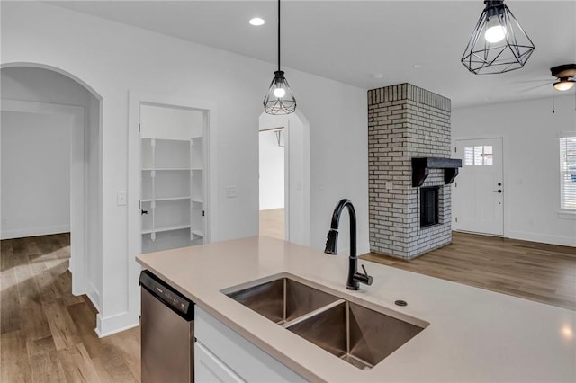 kitchen with dishwasher, sink, light hardwood / wood-style floors, decorative light fixtures, and a fireplace