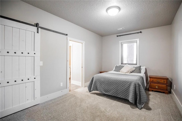 bedroom with light colored carpet, a barn door, and a textured ceiling