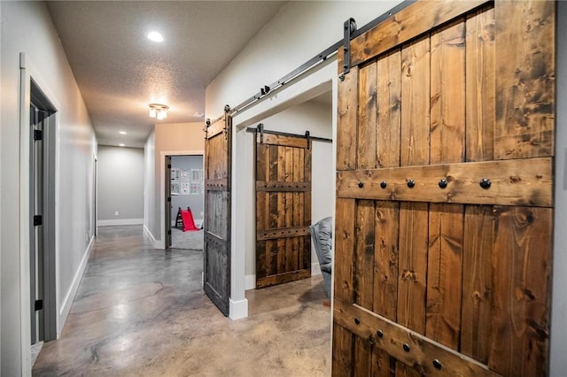 corridor with a barn door, concrete floors, and a textured ceiling