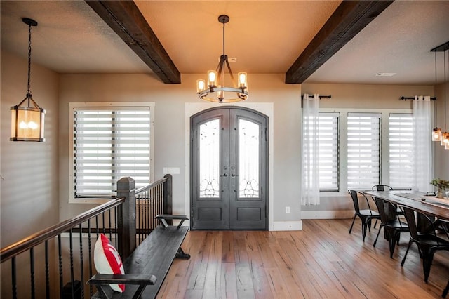 foyer entrance with french doors, beam ceiling, light wood-type flooring, and a notable chandelier