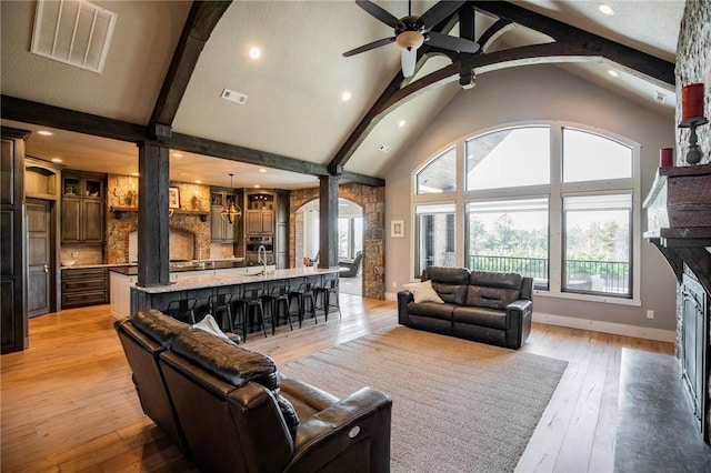 living room with light hardwood / wood-style flooring, ceiling fan, high vaulted ceiling, a fireplace, and beamed ceiling