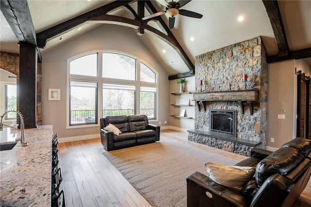 living room with sink, light hardwood / wood-style flooring, ceiling fan, vaulted ceiling with beams, and a stone fireplace