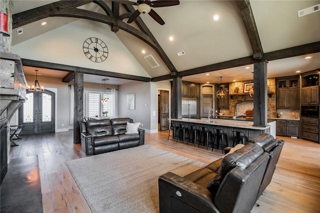 living room with ceiling fan with notable chandelier, beamed ceiling, decorative columns, light hardwood / wood-style floors, and french doors