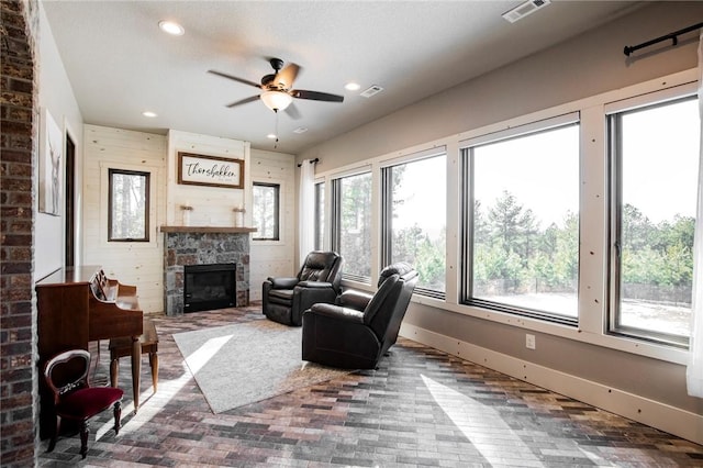 living room with ceiling fan, wooden walls, and a stone fireplace