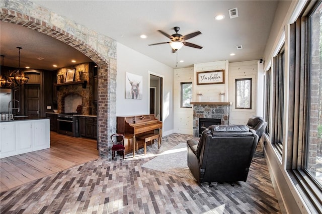 living room featuring hardwood / wood-style flooring, a stone fireplace, sink, and ceiling fan with notable chandelier