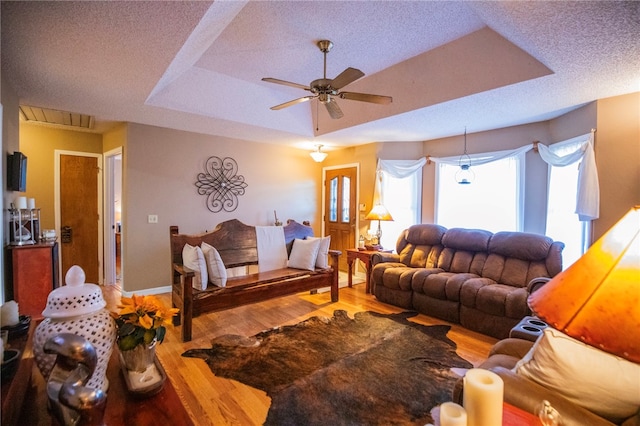 living room with a raised ceiling, ceiling fan, hardwood / wood-style floors, and a textured ceiling