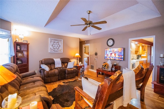 living room featuring light hardwood / wood-style floors, ceiling fan, a tray ceiling, and sink