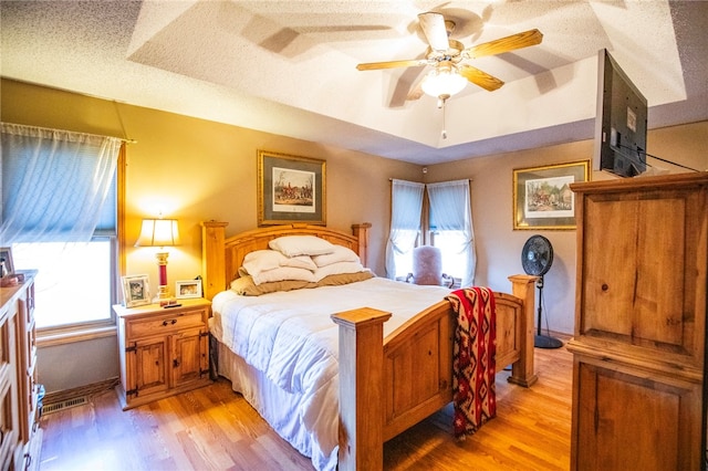 bedroom with ceiling fan, light wood-type flooring, a textured ceiling, and multiple windows