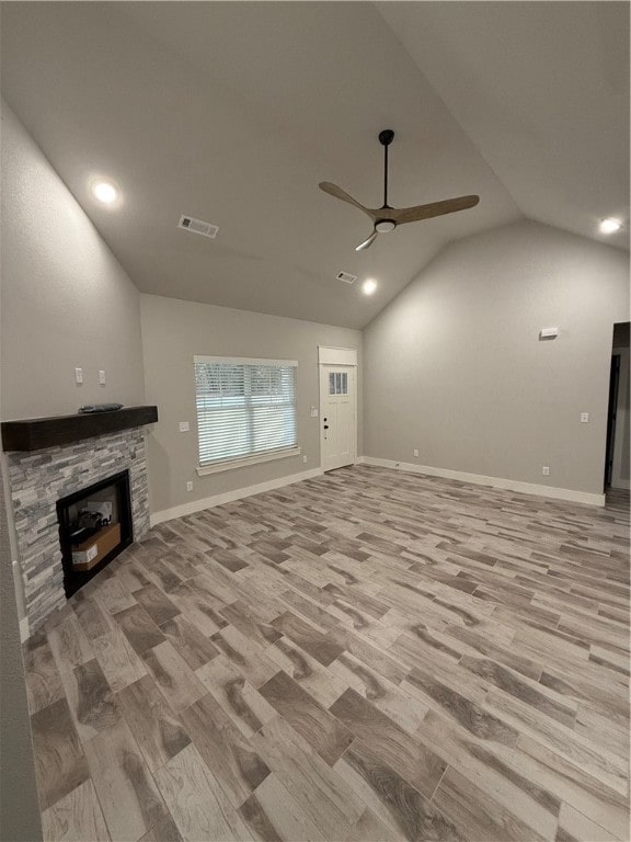 unfurnished living room with ceiling fan, a stone fireplace, lofted ceiling, and light wood-type flooring