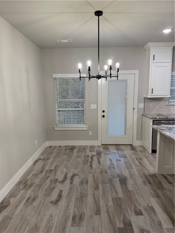 unfurnished dining area with a notable chandelier and light wood-type flooring